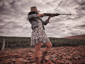 Full length of young woman holding rifle while standing against sky