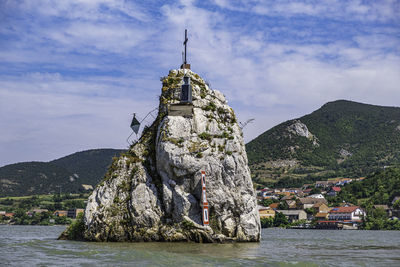 Cross on rock by sea and buildings against sky