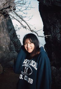 Portrait of smiling young woman standing by tree trunk