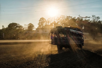 Vehicle moving on dirt road against sky during sunset