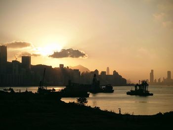 Silhouette buildings by sea against sky during sunset