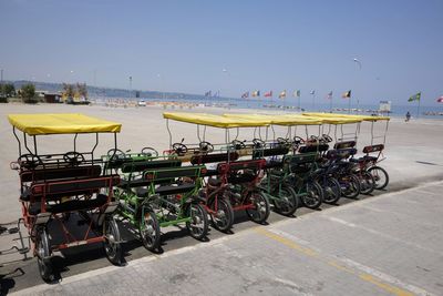 Pedicabs parked by footpath at beach against clear sky during sunny day