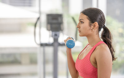 Determined young sportswoman in workout gear toning her arm muscles with a dumbbell.