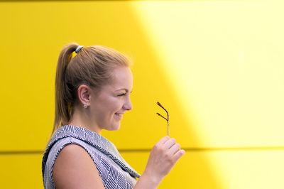 Smiling woman wearing eyeglasses by yellow wall