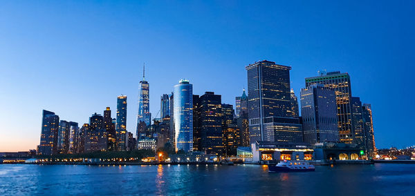 Illuminated buildings in city against clear blue sky