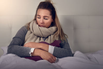 Sick woman sitting on bed at home