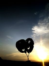Silhouette heart shaped balloons on field against sky during sunset