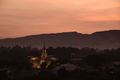 Silhouette buildings in city against sky during sunset