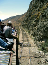 People sitting on roof by railroad track against sky