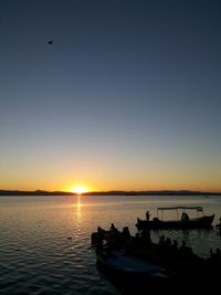 Silhouette boat in river against clear sky during sunset