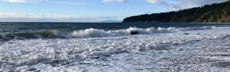 Waves rushing towards shore against sky
