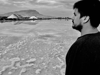 Side view of young man looking away in sea against sky