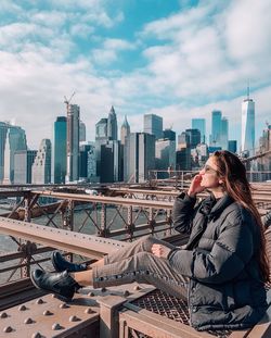 Woman sitting on modern buildings in city against sky
