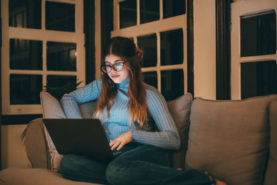 Young woman using laptop while sitting on sofa at home