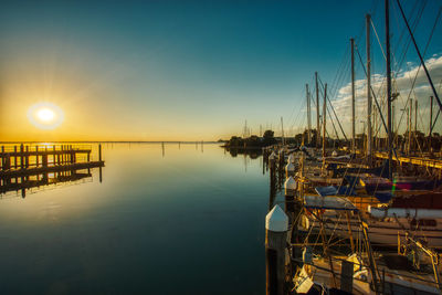 Boats moored in harbor at sunset