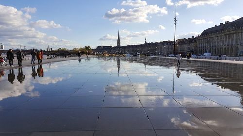 People walking on wet street in city against sky