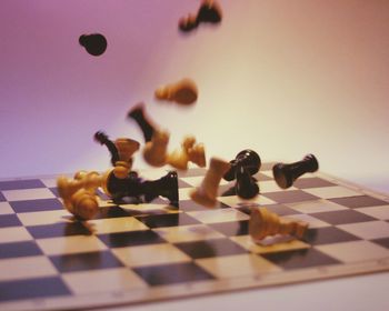 Close-up of chess piece falling on board falling against colored background