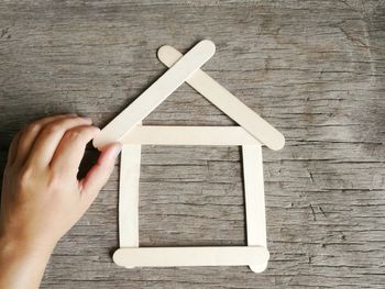 Cropped hand making model home with sticks on table