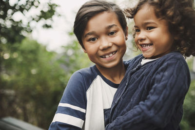 Portrait of happy boy carrying sister at yard