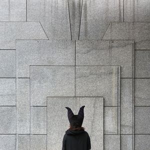Rear view of woman in animal mask in front of wall