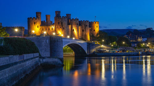 Illuminated castle and bridge over river against clear sky at night
