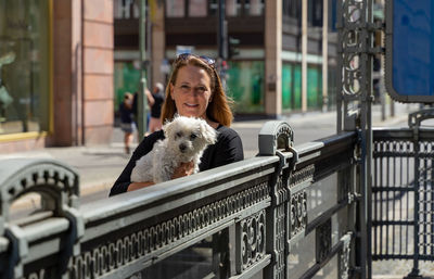 Portrait of woman with dog on railing in city