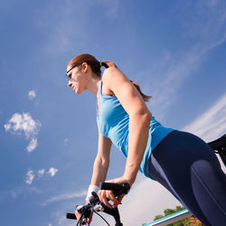 Low angle view of woman standing with bicycle against blue sky