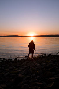 Man standing on rock at lakeshore against sky during sunset