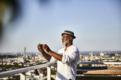 Mature man taking selfie while using smart phone standing on building terrace