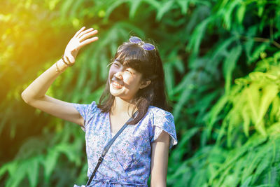 Smiling woman shielding eyes while standing against plants 