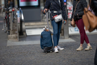 Low section of women with suitcase standing on street