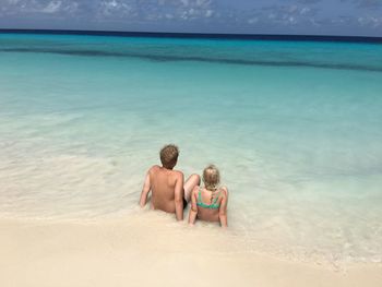 Rear view of siblings sitting on beach