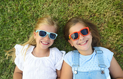 Portrait of smiling girls wearing sunglasses while lying on grass