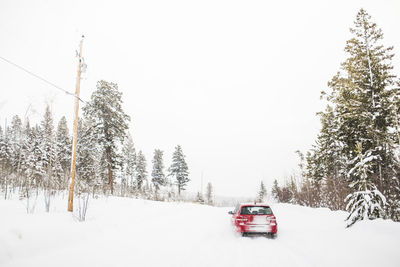 Rear view of red hatchback car driving on snow covered road.