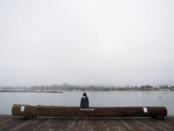 Rear view of man sitting on pier over lake against sky
