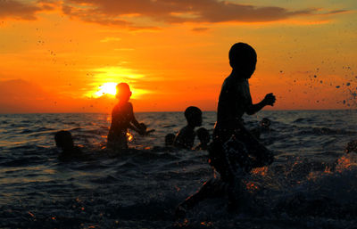 Silhouette of children playing in the ocean at sunset