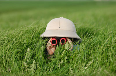 Boy in sun hat looking through binoculars on field