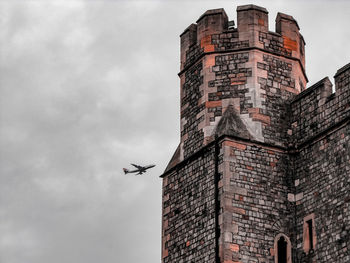 Low angle view of airplane flying by building against sky