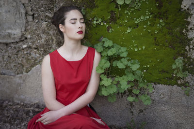 Young woman looking away while sitting against wall