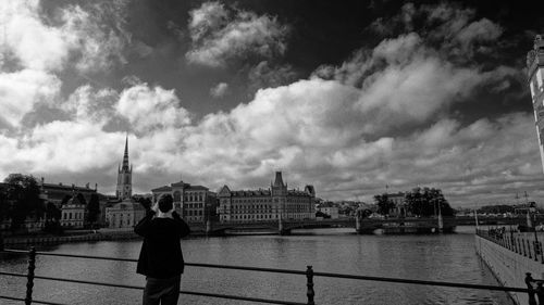 Rear view of man standing on bridge over river against cloudy sky