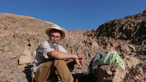 Senior man sitting on rock against mountain in desert 