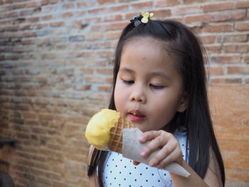 Portrait of girl holding ice cream against wall