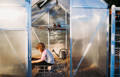 Young girl sitting in backyard greenhouse planting seeds in spring