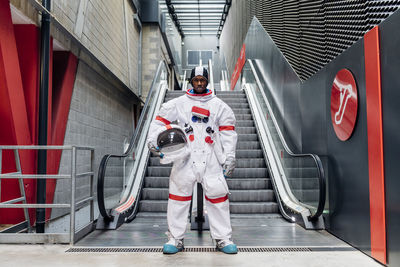 Mid adult man holding space helmet while standing in front of escalator