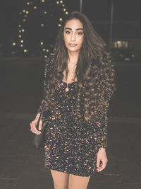 Portrait of woman standing on footpath at night