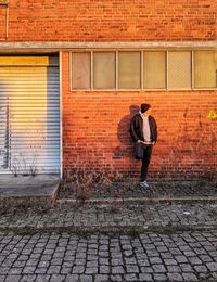 Full length of man standing on footpath against brick wall