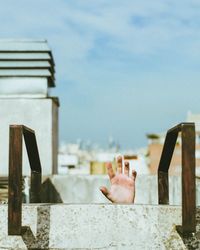 Cropped hand of person asking for help seen through tank against sky