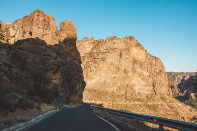 Road leading towards rocky mountains against clear sky