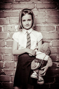 Portrait of girl standing with stuffed toy against brick wall