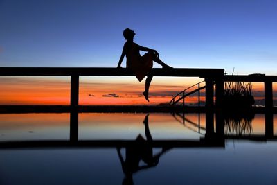 Silhouette woman on railing reflecting in water during sunset